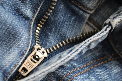 Primer plano detallado de una cremallera de jean azul con la marca YTR visible, mostrando la textura del denim.