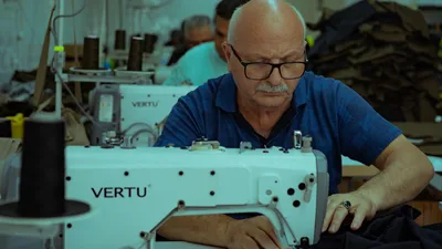 Sastre anciano se concentra en la costura de prendas con una máquina en su taller de Ankara